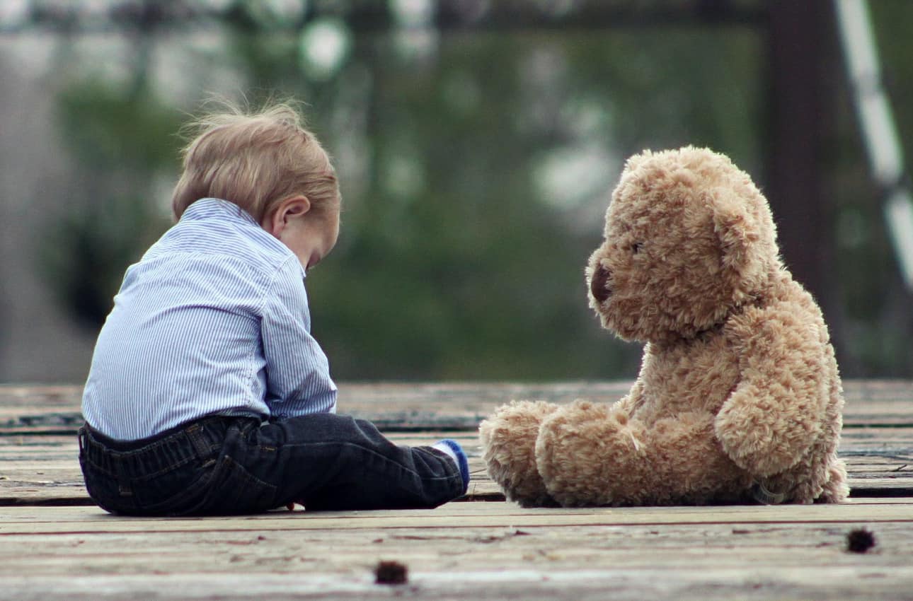 Billede af barn der sidder på en træterrasse sammen med sin bamse