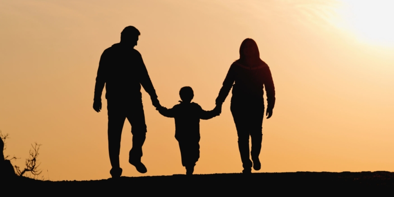 Silhuetter i solnedgangslys barnmed mor og far, set bagfra